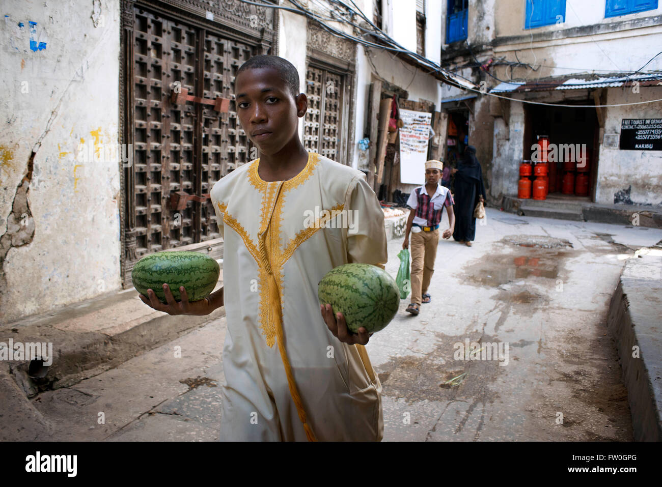 Homme avec un deux melons d'eau à côté du teck massif portes de l'une chambre à Stone Town s labyrinthe de rues étroites, Zanzibar, Tanzan Banque D'Images