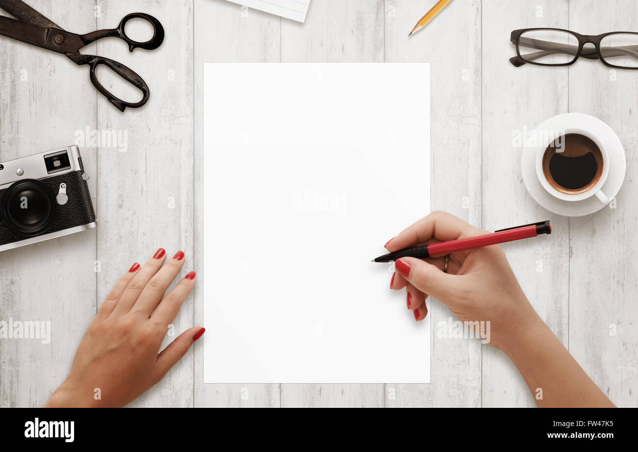 Femme écrire avec stylo rouge sur papier blanc, isolé. Le café, lunettes, appareil photo, bloc-notes, crayon sur table en bois. Vue d'en haut. Banque D'Images