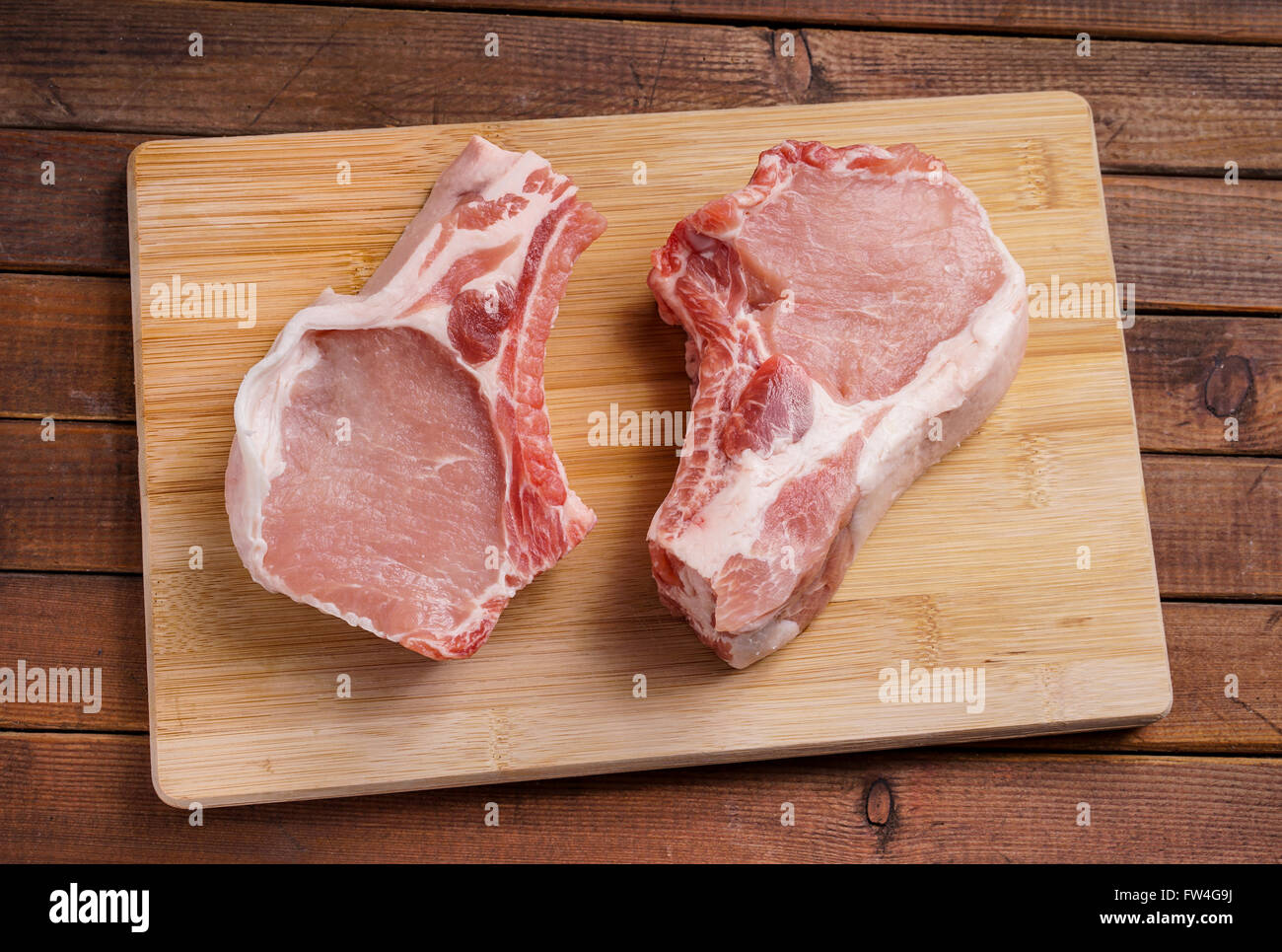 Côtelettes de porc cru, allongé sur une planche de bois pour la cuisson Banque D'Images