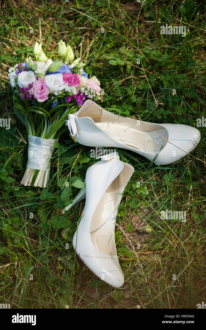 Paire de chaussures dames blanc sur l'herbe et joli bouquet de fleurs. Accessoires de mariage. Banque D'Images