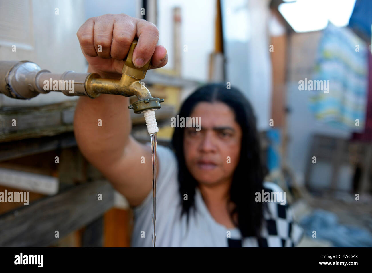 Robinet d'ouverture de la femme utilisé conjointement réservoir d'eau, l'assainissement des taudis Favela 21 de Abril, São Paulo, Brésil Banque D'Images