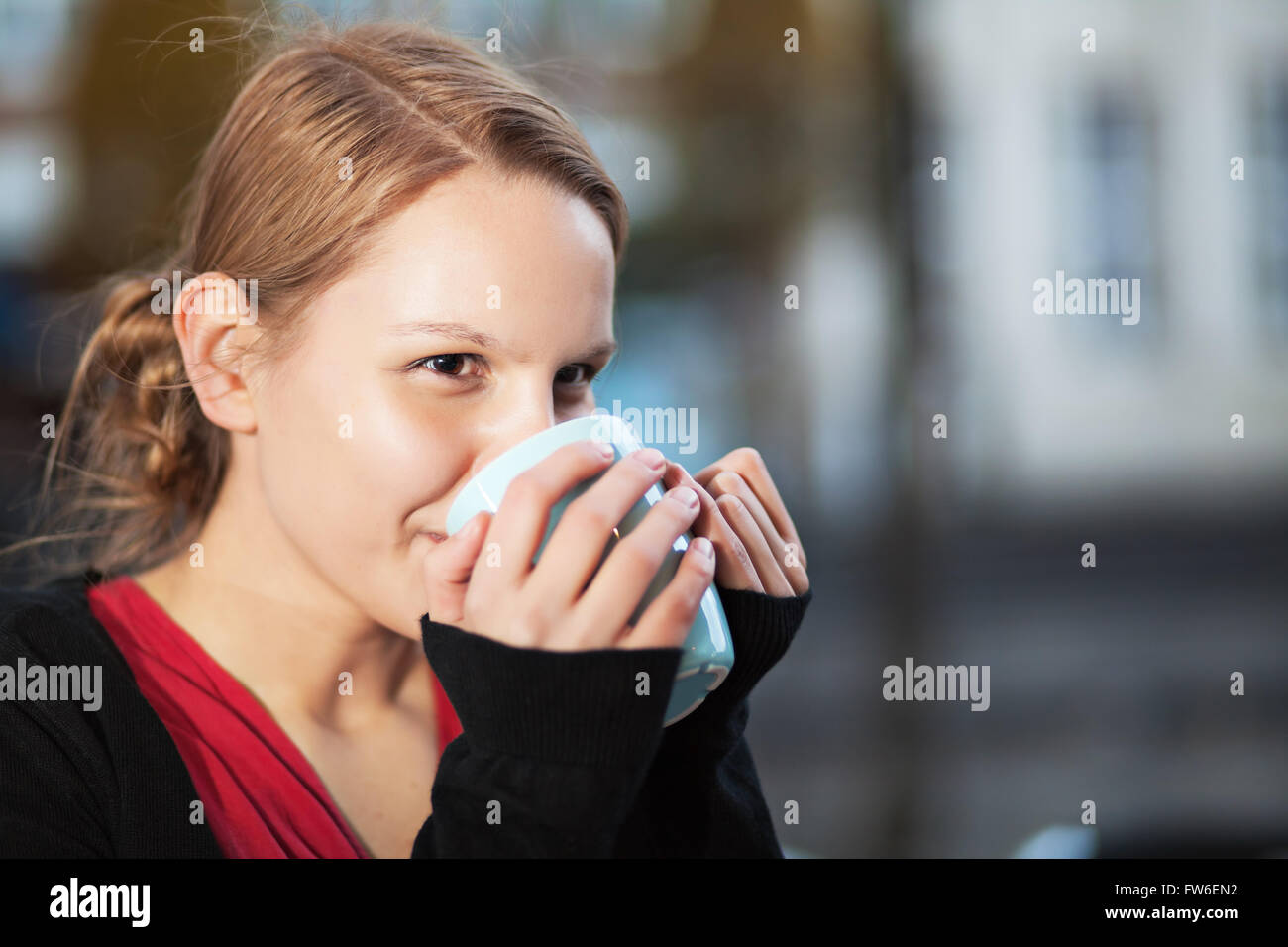 Jolie jeune femme à boire une boisson chaude dans une tasse en céramique à l'extérieur Banque D'Images