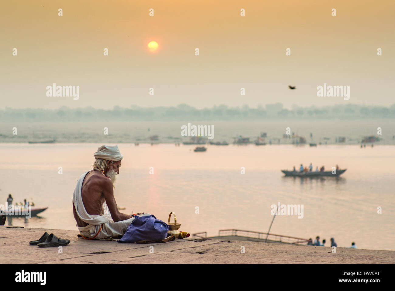 Un sadhu (dévot hindou) est assis par le fleuve saint Ganges à Varanasi comme le soleil se lève à l'arrière-plan. Banque D'Images