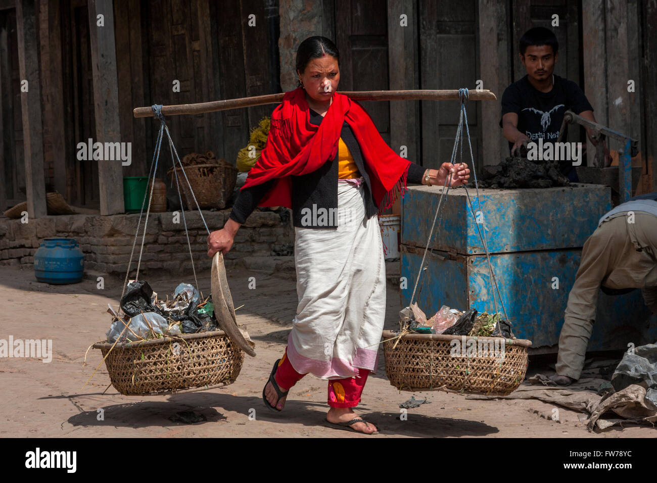 Bhaktapur, Népal. Newari Femme portant des paniers à l'aide de poteau de l'épaule (LNO). Traditionnellement les femmes de Bhaktapur porter du rouge et noir. Banque D'Images