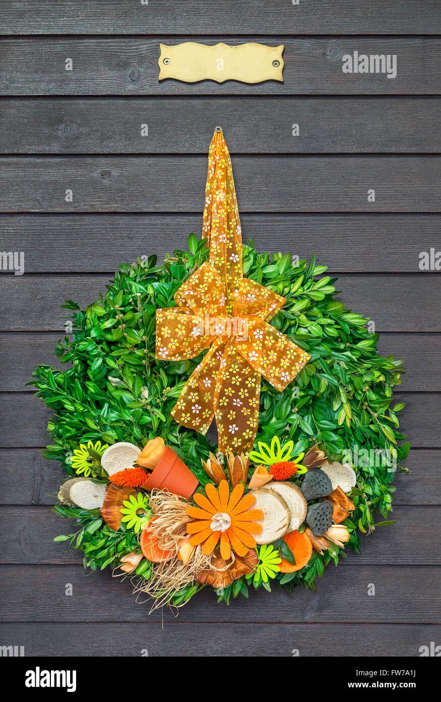 Couronne de printemps avec orange arc accroché sur la porte en bois foncé avec plaque Banque D'Images