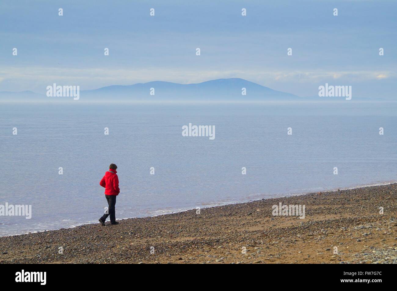 Lonely Woman walking on beach avec Criffel à distance. Allonby, Cumbria, Angleterre, Royaume-Uni, Europe. Banque D'Images