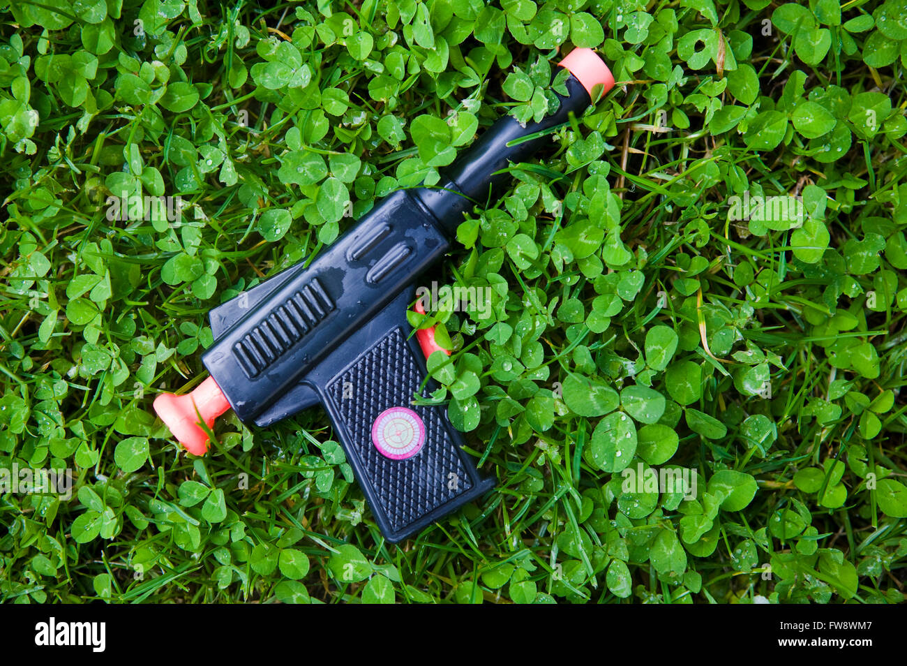Un pistolet d'enfant ou en plastique pistolet jouet laissé allongé dans  l'herbe d'un jardin, perdu dans le trèfle l'arme représente un jouet à  l'enfant même si certains peuvent croire que l'utilisation de