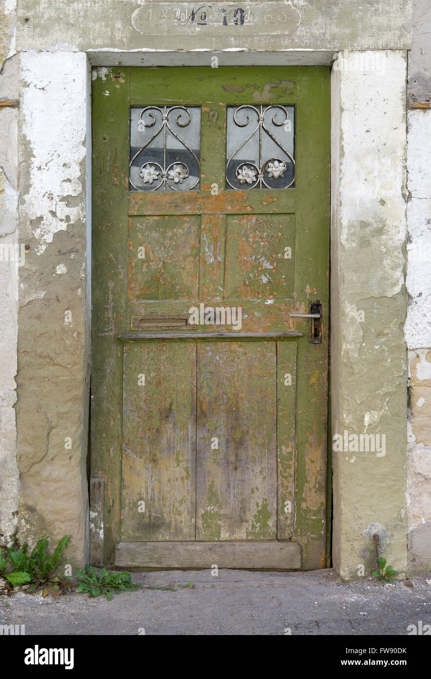 Ancien, vert, porte en bois patiné avec deux petits panneaux de verre interdit dans la façade délabrée d'une maison abandonnée. Banque D'Images
