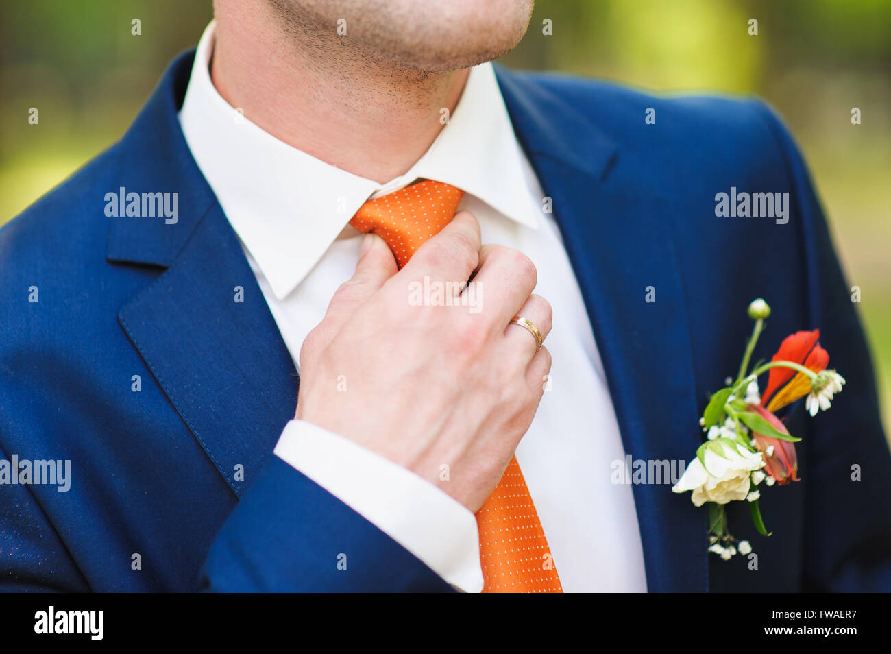 Marié en chemise blanche et costume bleu la correction d'une cravate orange.  Anneau sur son doigt. Belle boutonnière du marié costume sur. L'homme à b  Photo Stock - Alamy