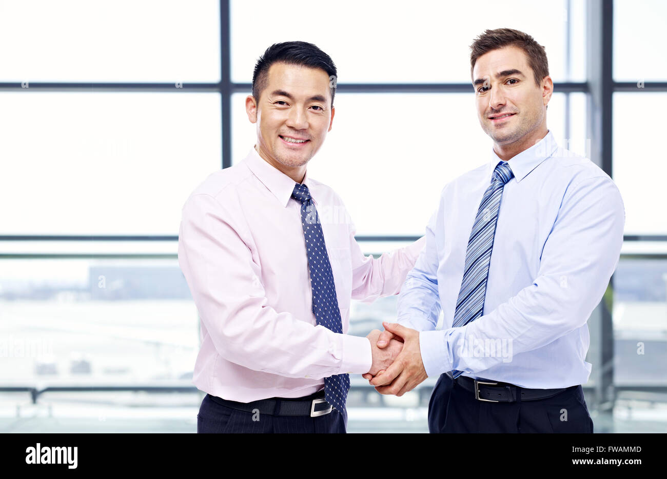 Asian and Caucasian businessmen shaking hands at airport. Banque D'Images