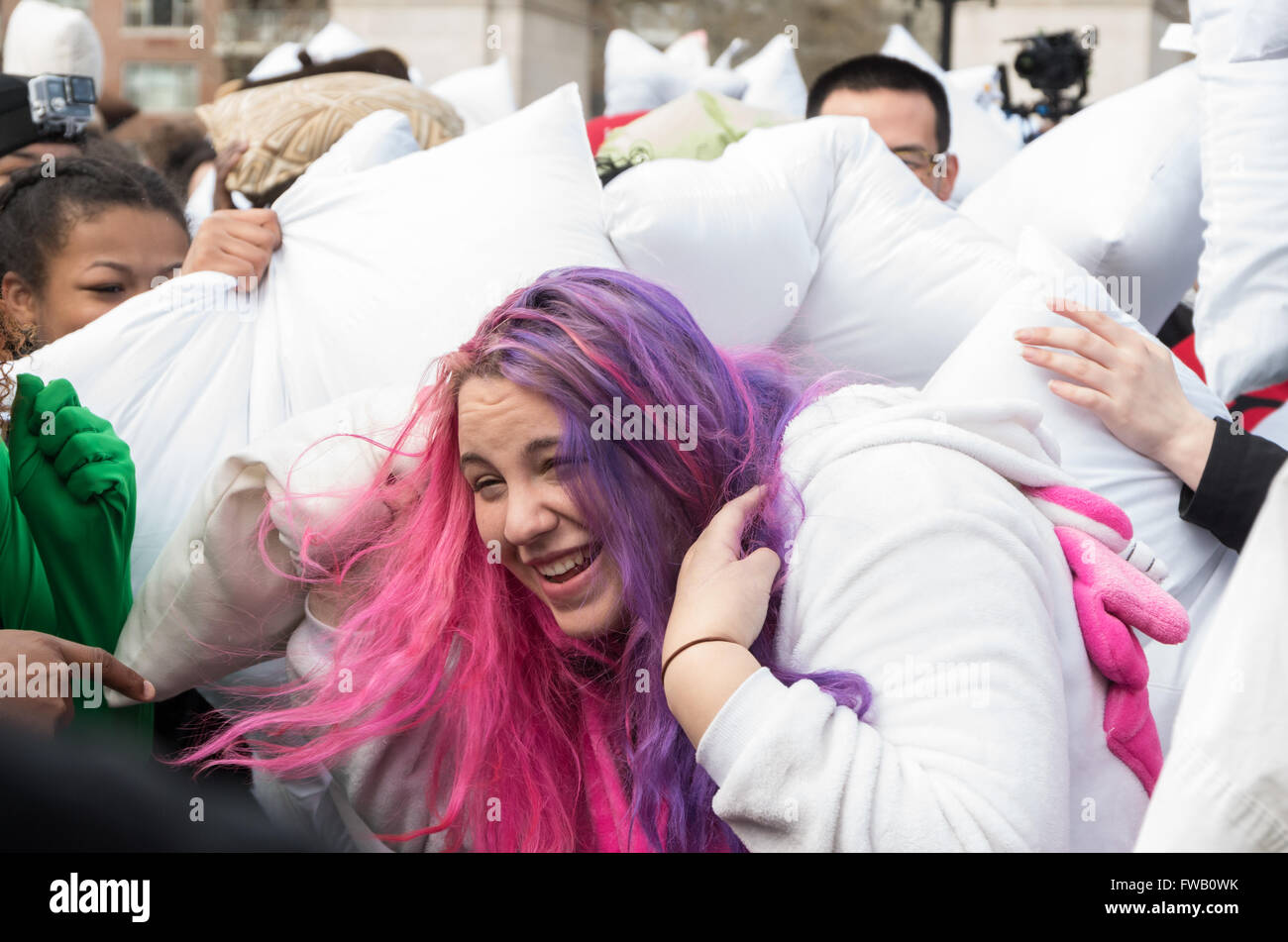 Jeune femme / fille aux cheveux rose et pourpre d'être frappé par de nombreux oreillers et de rire dans la plus grande guerre d'oreillers à Washington Square Park, New York. Banque D'Images