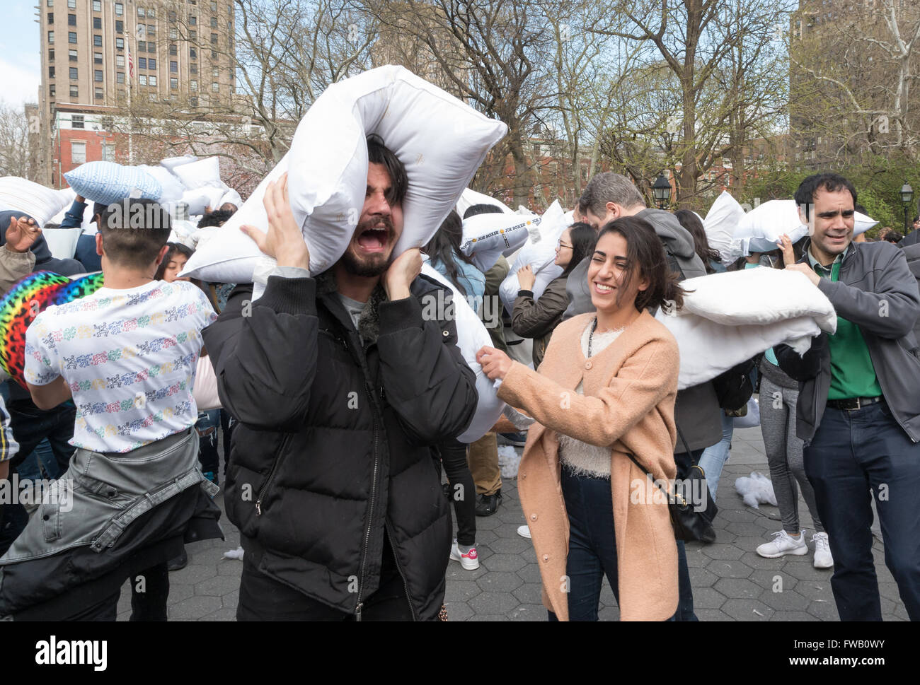 Jeune homme barbu tenant un oreiller sur sa tête et les simulacres de pleurer comme une jeune femme le frappe avec un oreiller pendant la plus grande guerre d'oreillers à Washington Square Park, New York Banque D'Images