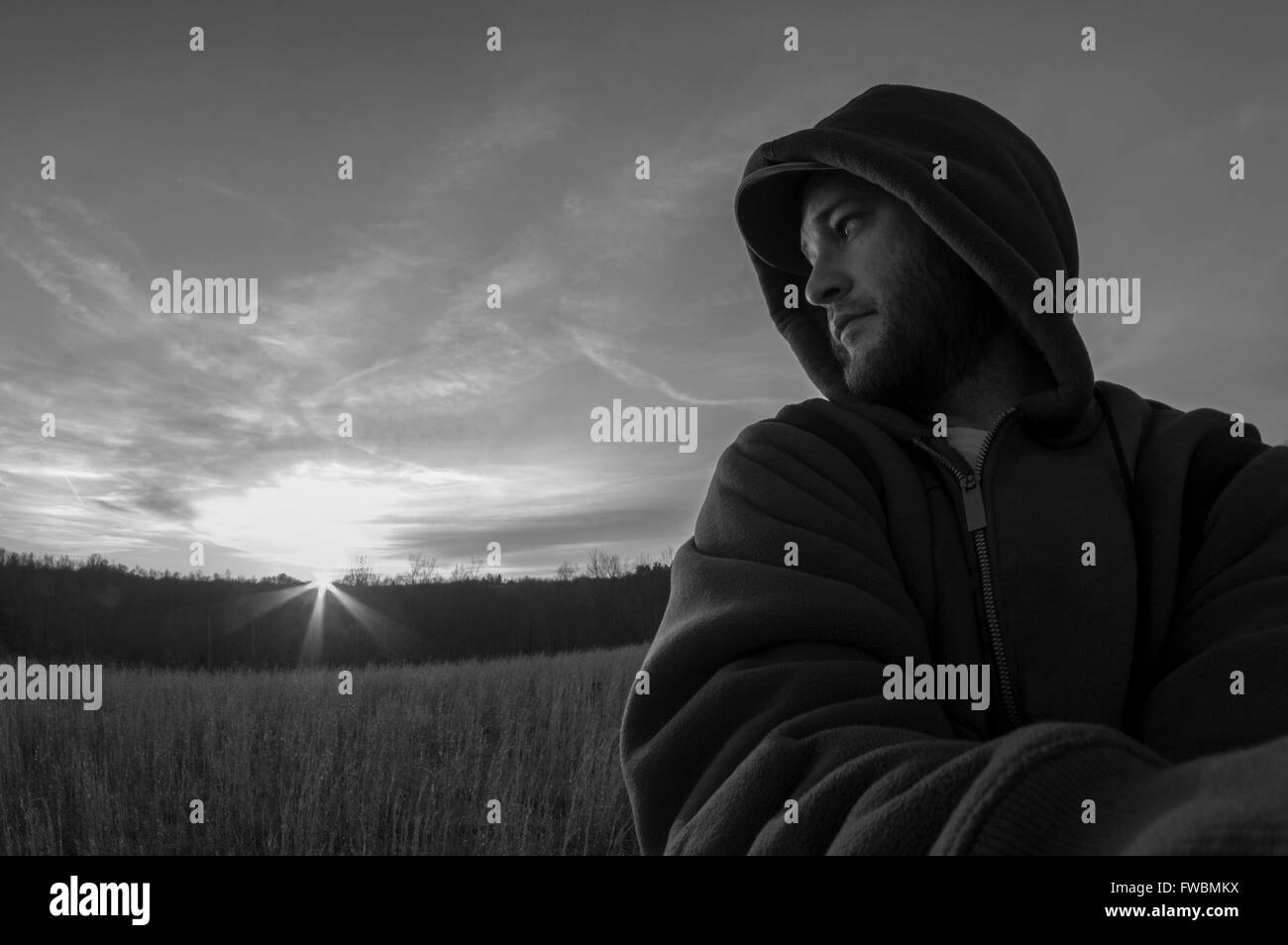 Self portrait noir et blanc d'un homme debout, dans un champ à l'extérieur regardant par-dessus son épaule vers le soleil. Banque D'Images