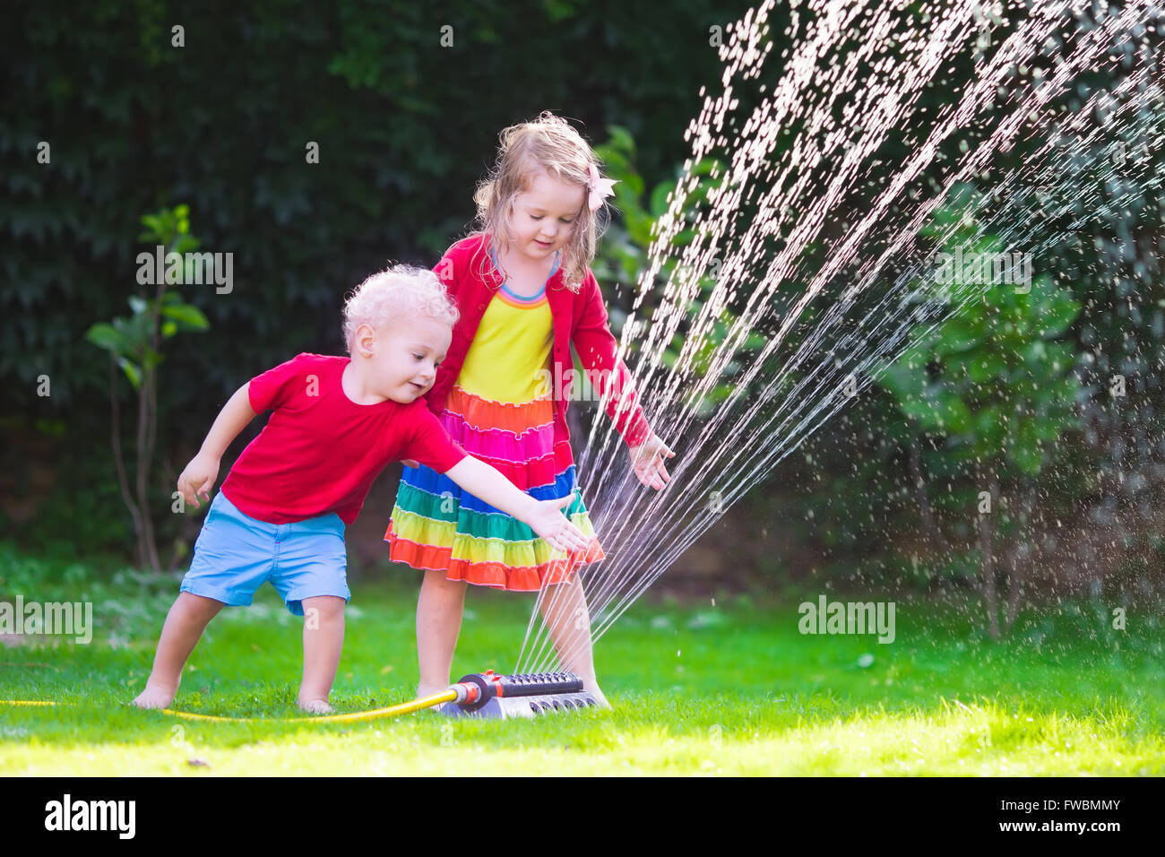 Enfant jouant avec jardin arroseur. Enfant d'âge préscolaire la course et le saut. Piscine d'été de plaisir de l'eau dans la cour. Banque D'Images