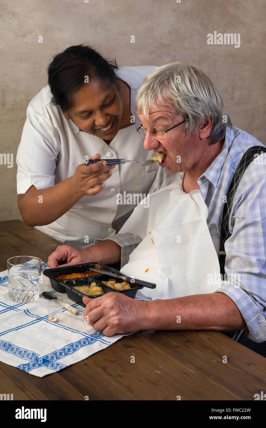 Infirmière en maison de retraite à essayer de faire manger son dîner d'un patient Banque D'Images