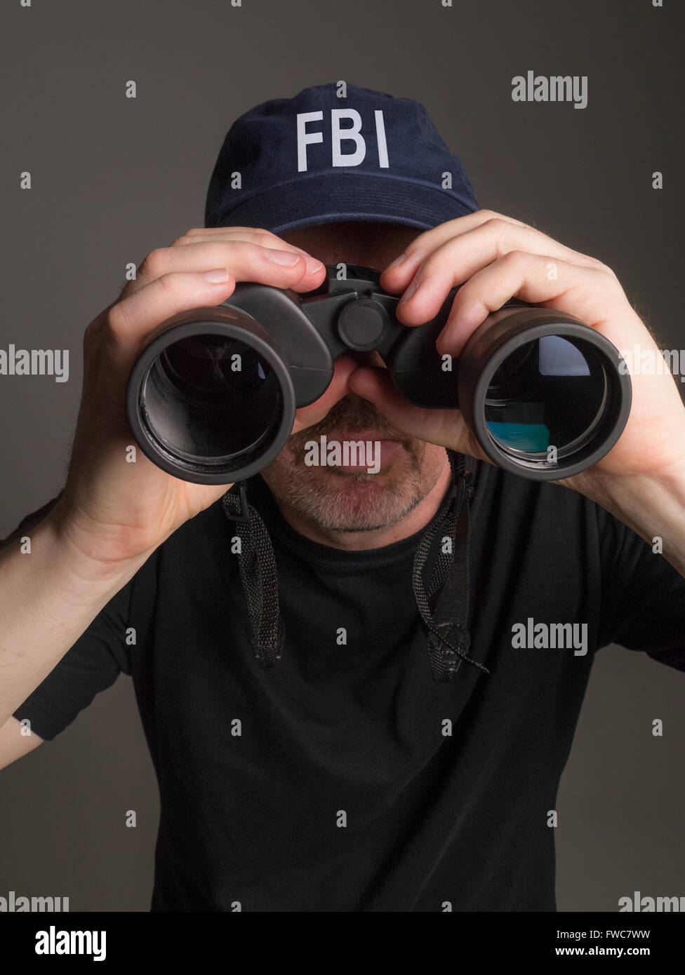 Photographie d'un agent du FBI en noir T-shirt et casquette de regarder à travers les jumelles. Banque D'Images