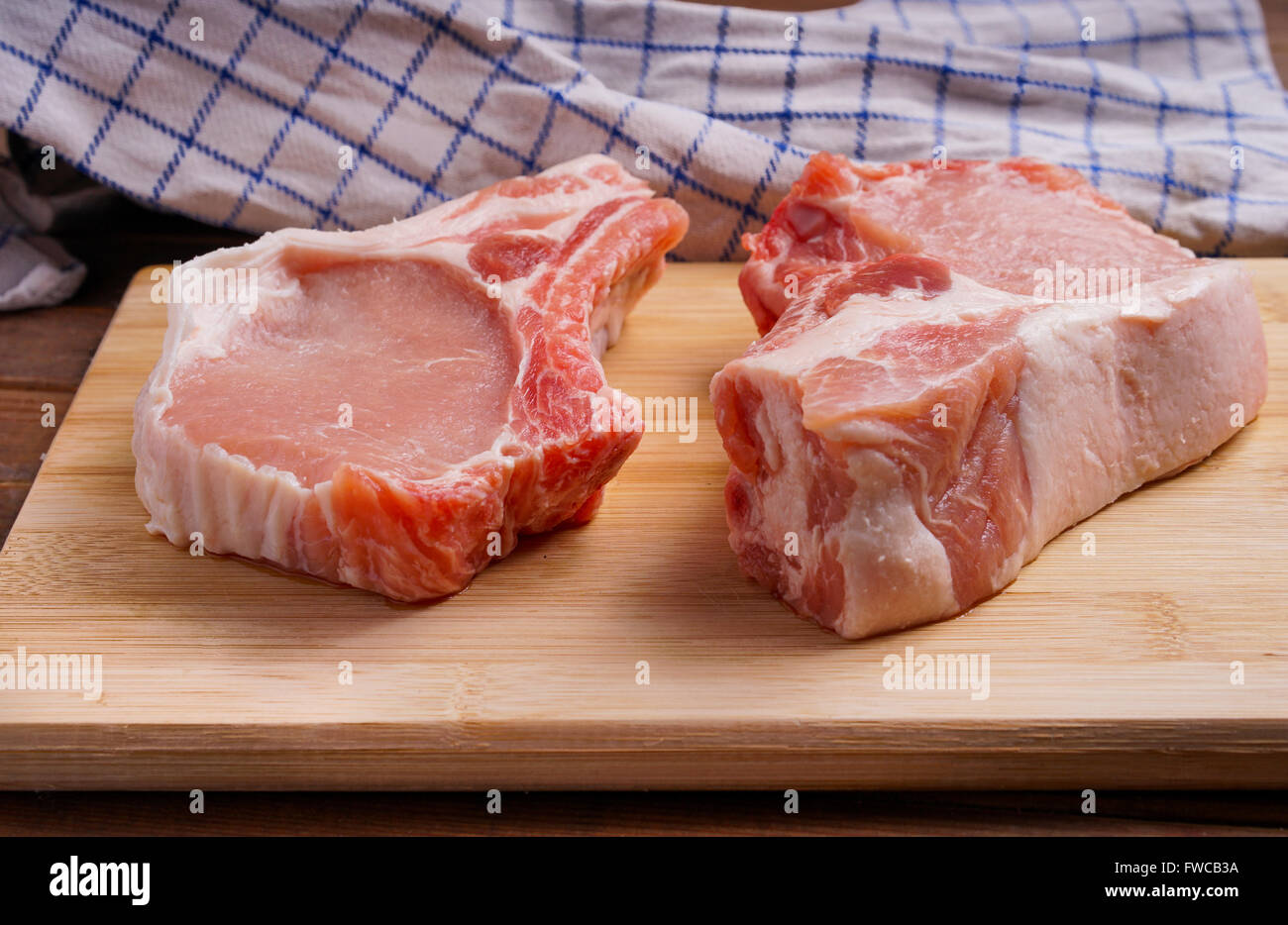 Côtelettes de porc cru, allongé sur une planche de bois pour la cuisson Banque D'Images