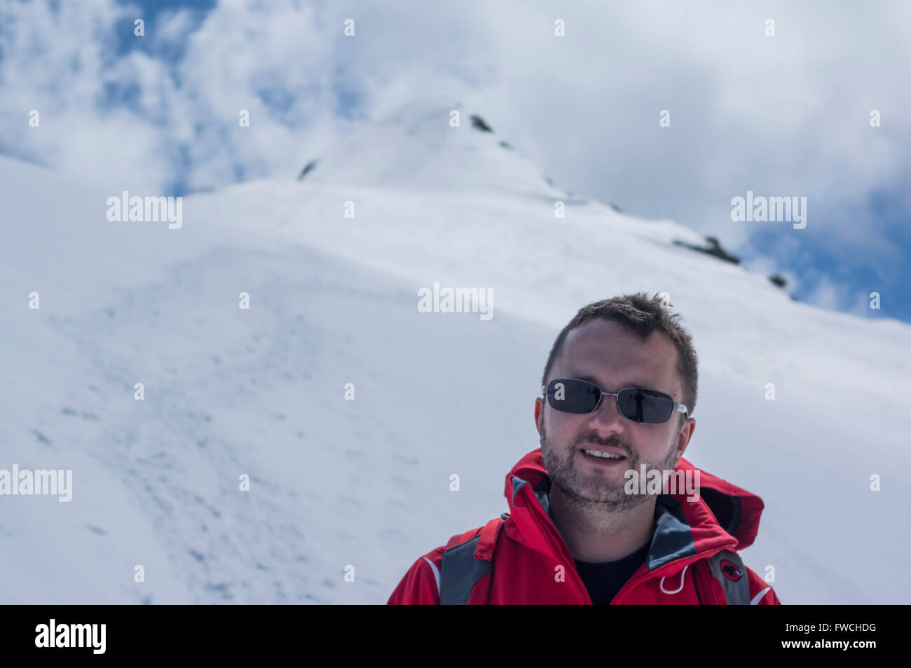 Jeune homme de race blanche portant une veste rouge en face d'une montagne enneigée dans les Alpes suisses. Canton d'Uri, en Suisse. Banque D'Images