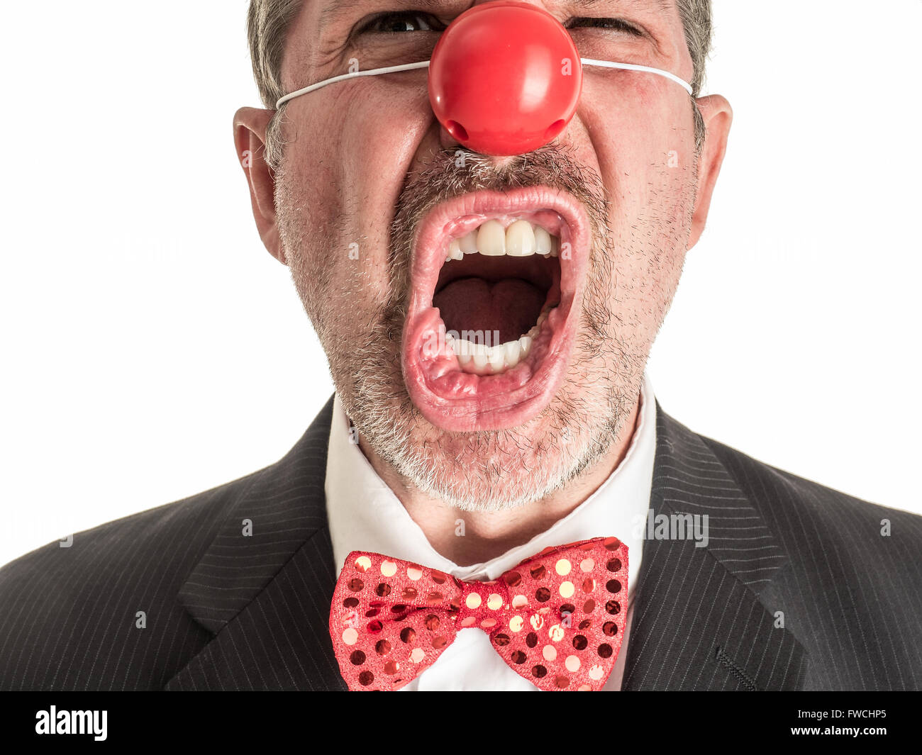 Photo Gros plan d'un homme en costume avec un nez en caoutchouc rouge et un nœud Papillon rouge brillant crier vers la caméra. Banque D'Images