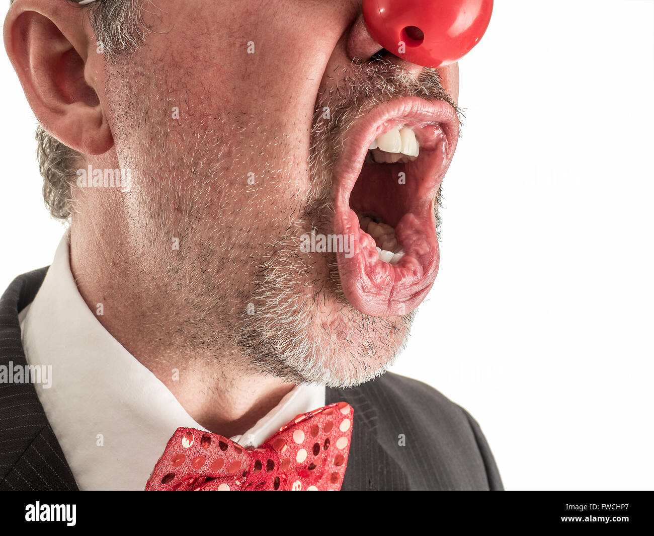 Photo Gros plan d'un homme en costume avec un nez en caoutchouc rouge et noeud papillon rouge brillant crier au sommet de ses poumons. Banque D'Images