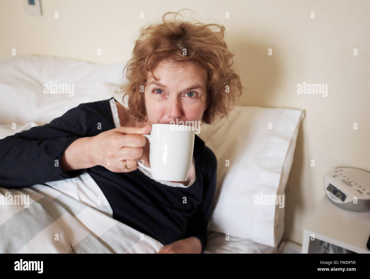 Femme à la tasse de thé potable échevelée après le réveil le matin au lit Banque D'Images