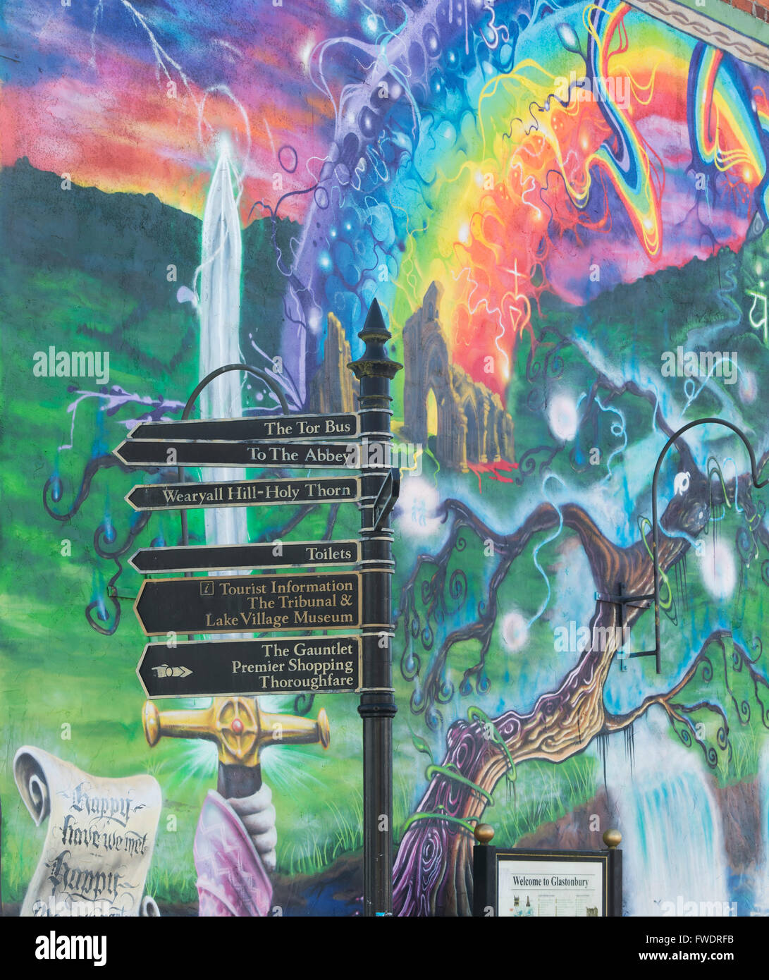 Des panneaux de direction touristique devant une murale colorée. Glastonbury, Somerset, Angleterre. Banque D'Images