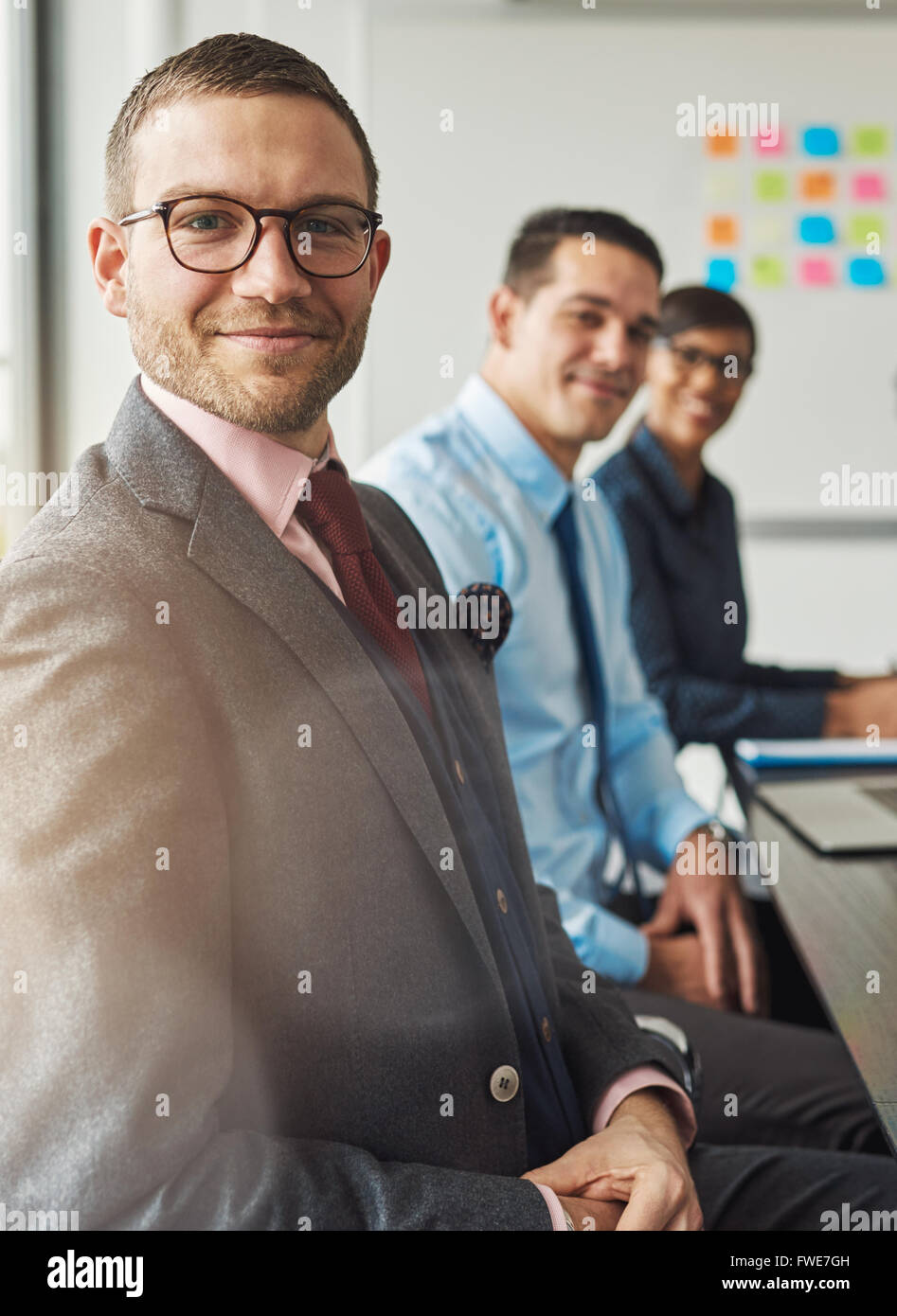 Beau barbu portant costume et cravate avec deux collègues de la direction en réunion à la table de conférence en face de grand blanc Banque D'Images