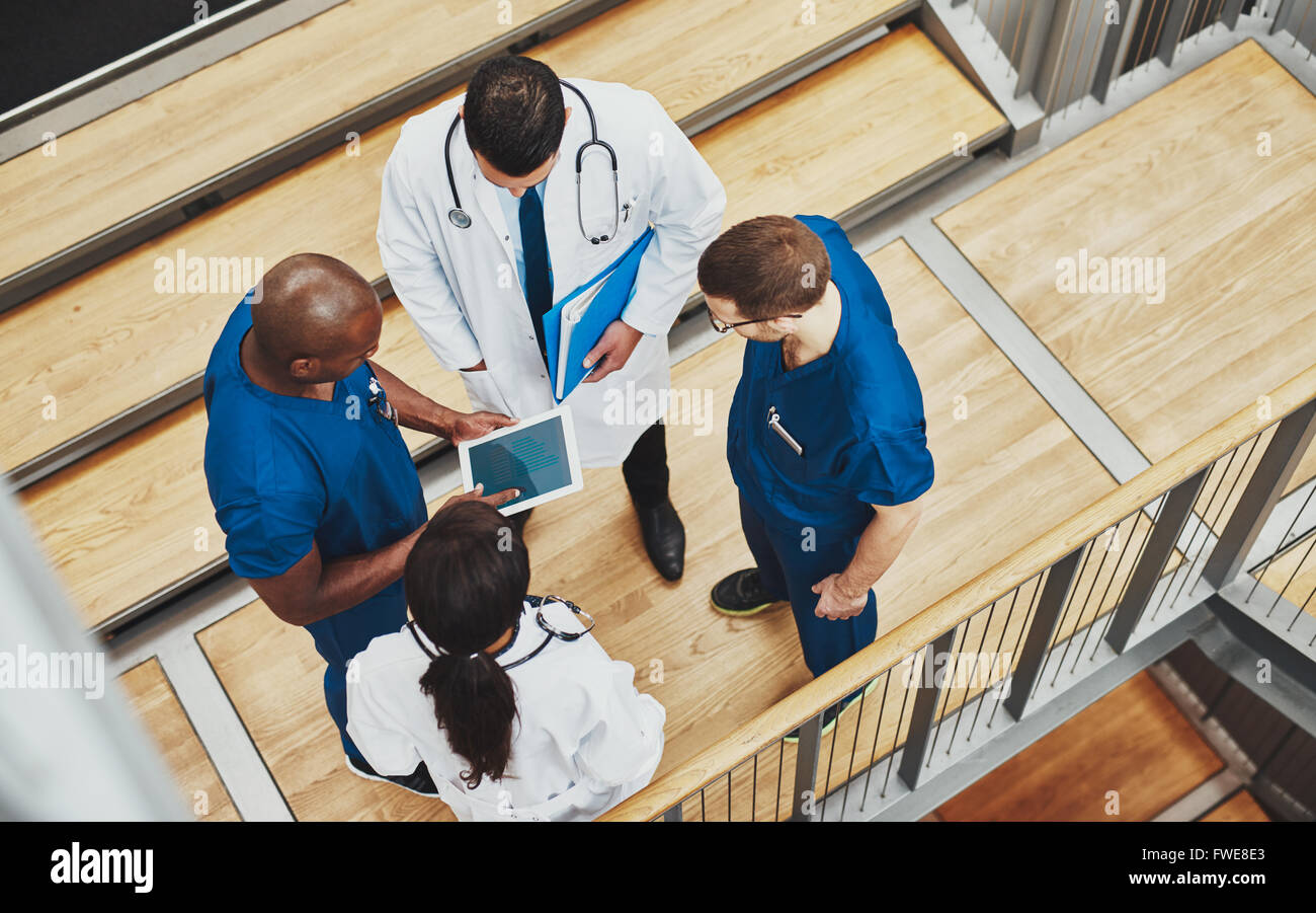 L'équipe médicale multiraciale d'avoir une discussion en l'état regroupés autour d'un ordinateur tablette sur un escalier, les frais généraux et v Banque D'Images
