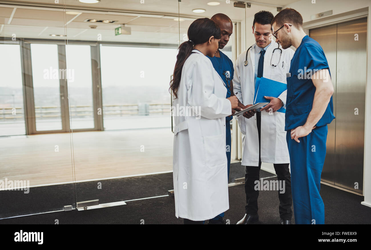 L'équipe médicale multiraciale diverses consultations sur un dossier patient debout dans un hall d'accueil à l'hôpital regroupées autour d'une tablette compu Banque D'Images