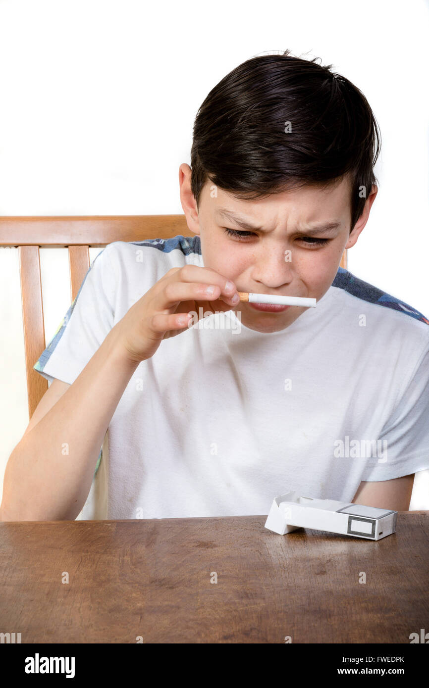 Jeune garçon curieux reniflant une cigarette avec un regard de dégoût Banque D'Images