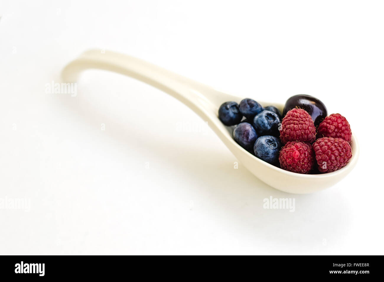 Cuillère en céramique plein de framboises,cerises et bleuets isolé sur blanc. Banque D'Images