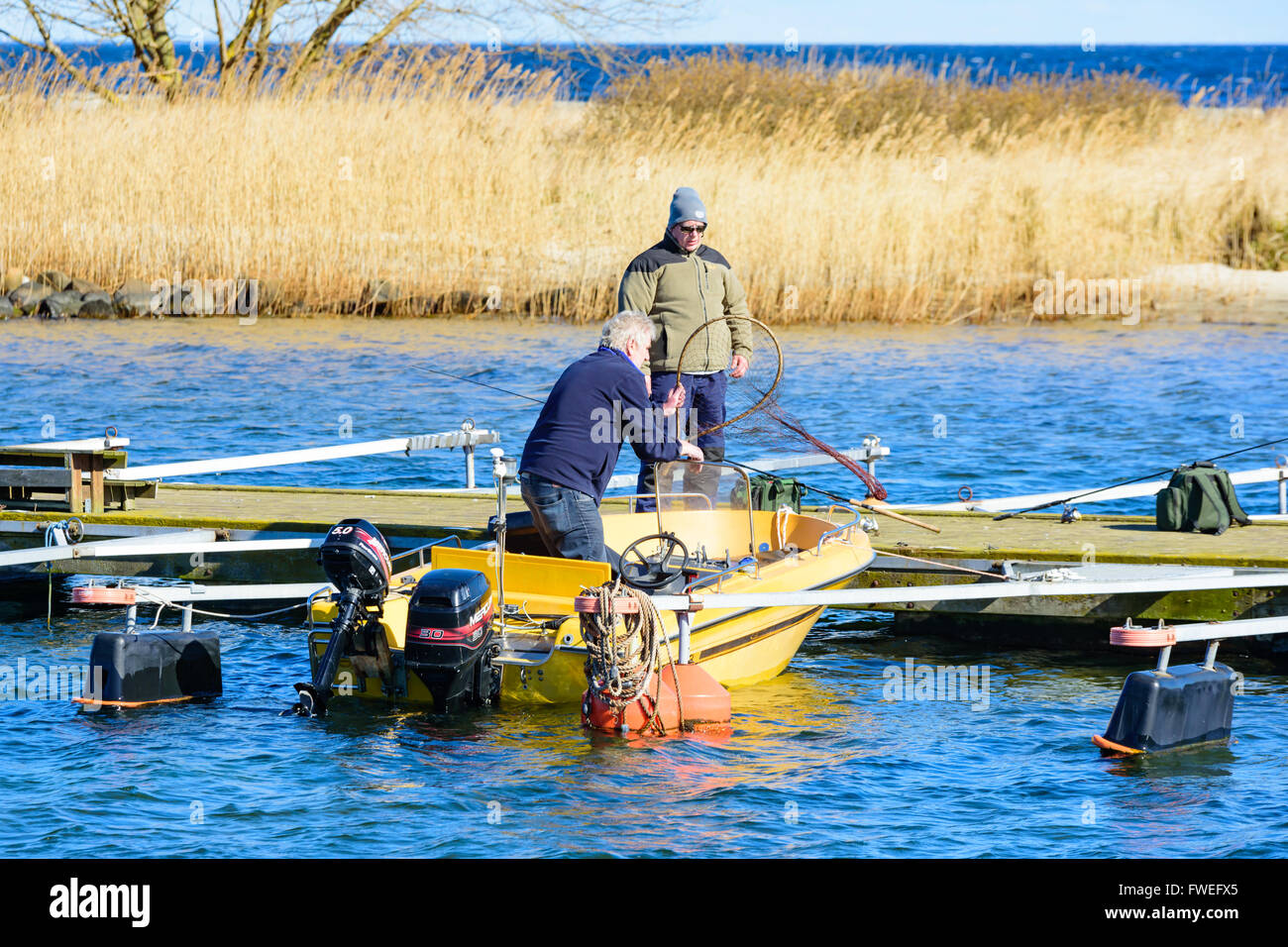 Kivik, Suède - 1 Avril 2016 : deux hommes se préparent à prendre un bateau jaune dehors pour un peu de pêche. Une personne debout sur la pi Banque D'Images