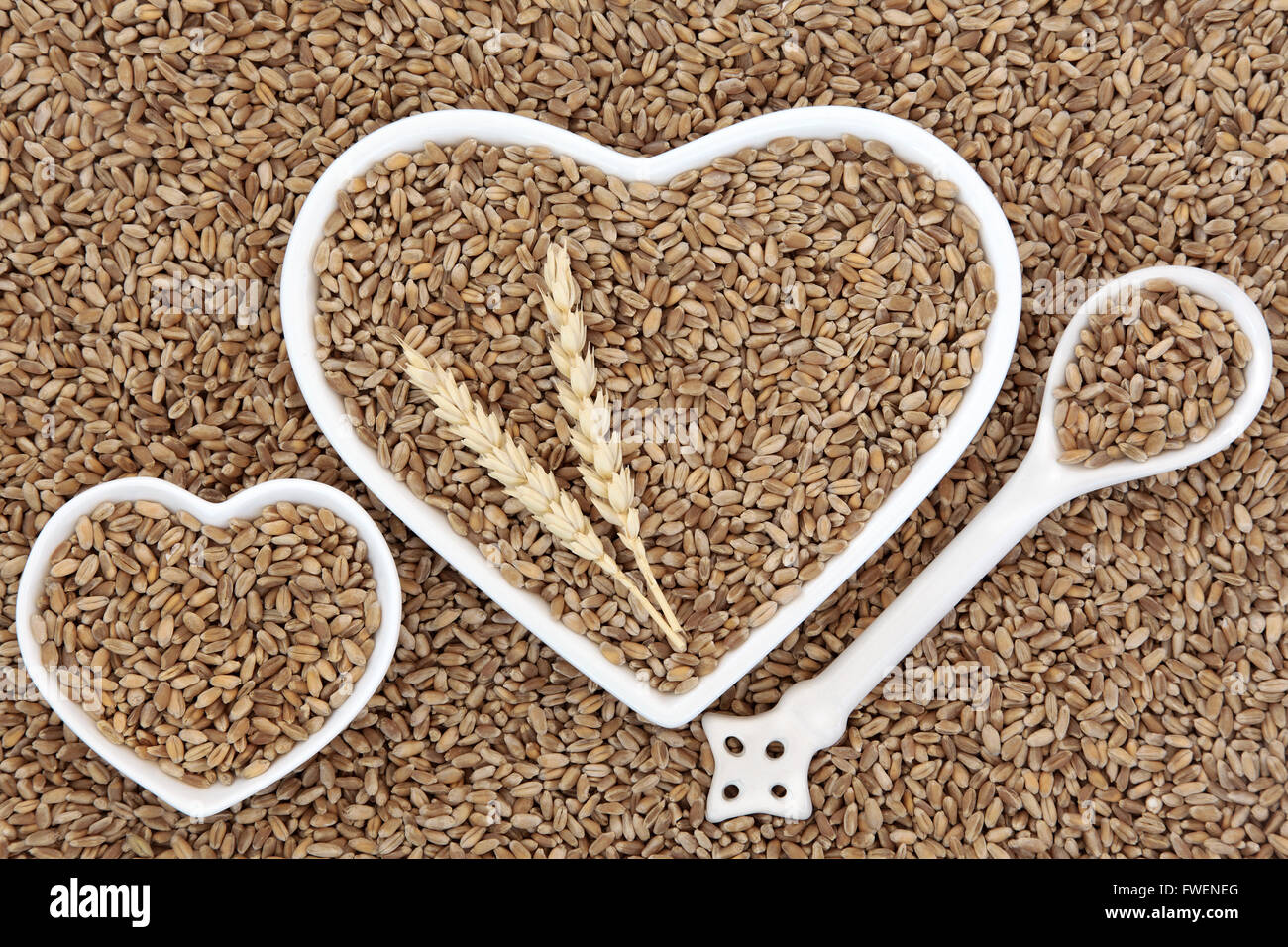 Le grain de blé dans l'alimentation des bols en forme de coeur et cuillère en porcelaine avec les gaines formant un motif de fond. Banque D'Images