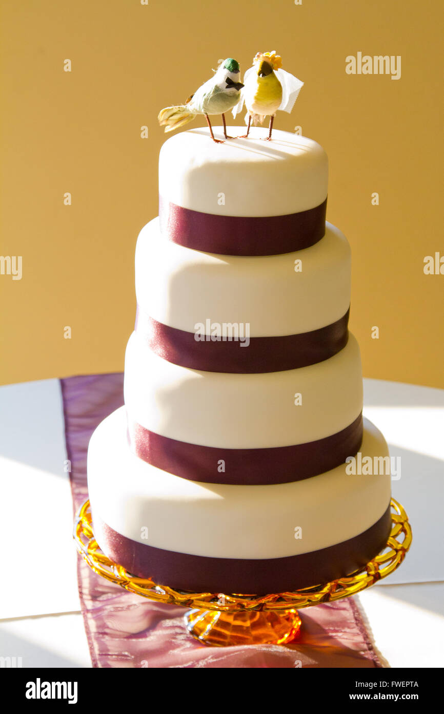 Un gâteau de mariage traditionnel blanc est surmonté d'oiseaux artisanat et enveloppés dans du ruban violet chez la mariée et la réception. Banque D'Images