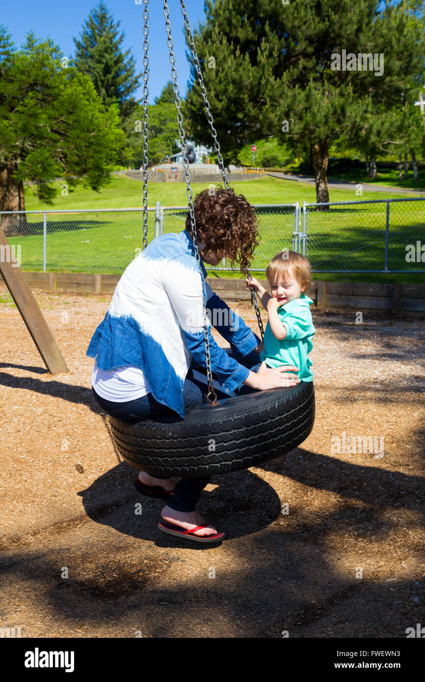 Un fils et sa maman partagent une balançoire pneu sur l'aire d'un parc dans l'Oregon. Banque D'Images
