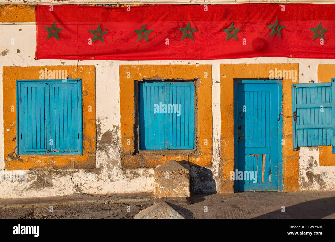 Les volets bleus des fenêtres et portes bleu orange avec les cadres. Vieille maison à Essaouira. Longue bande de drapeau marocain. Banque D'Images