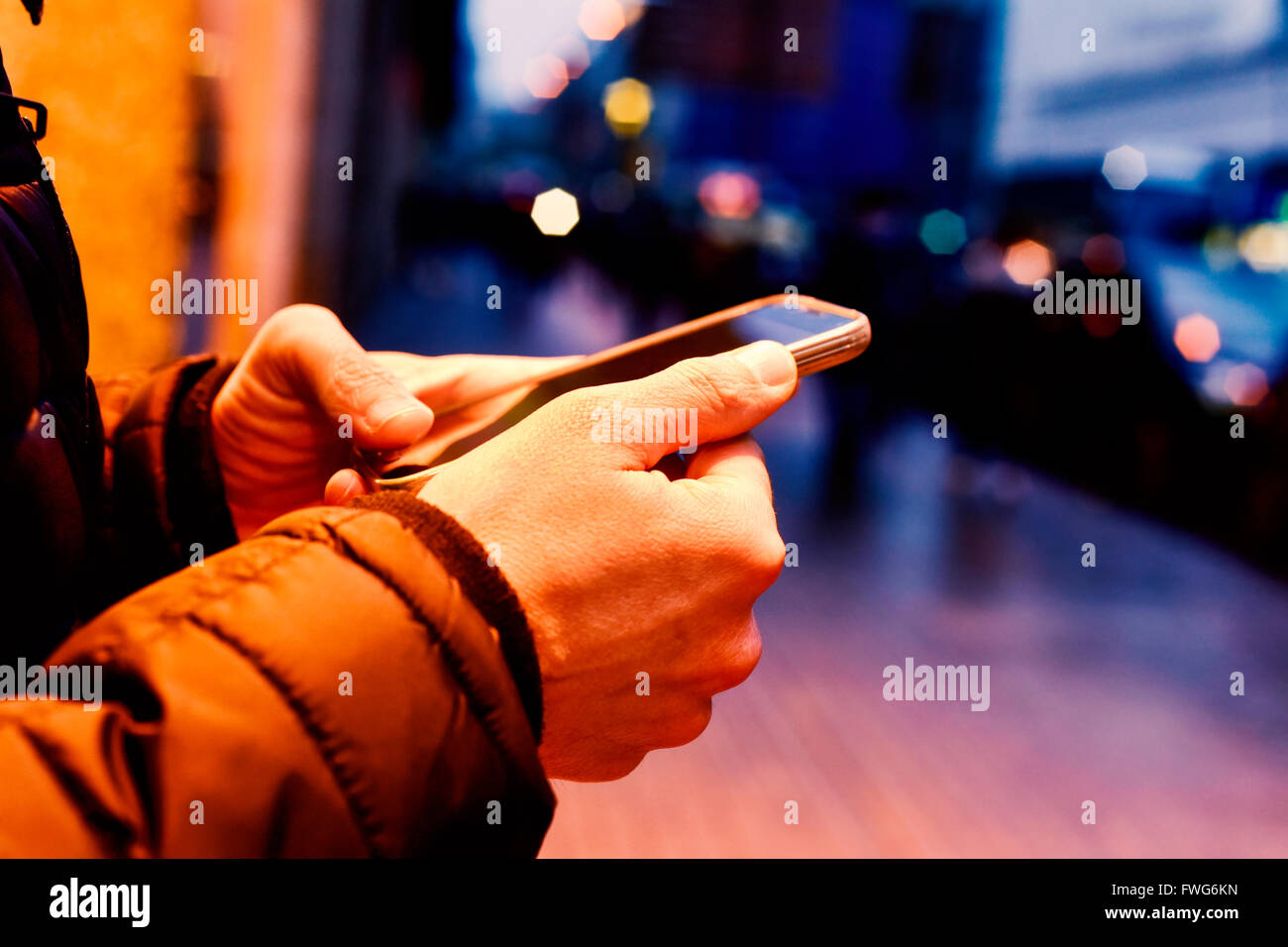 Closeup of a young caucasian man wearing a Down jacket utilise son smartphone dans la rue la nuit Banque D'Images