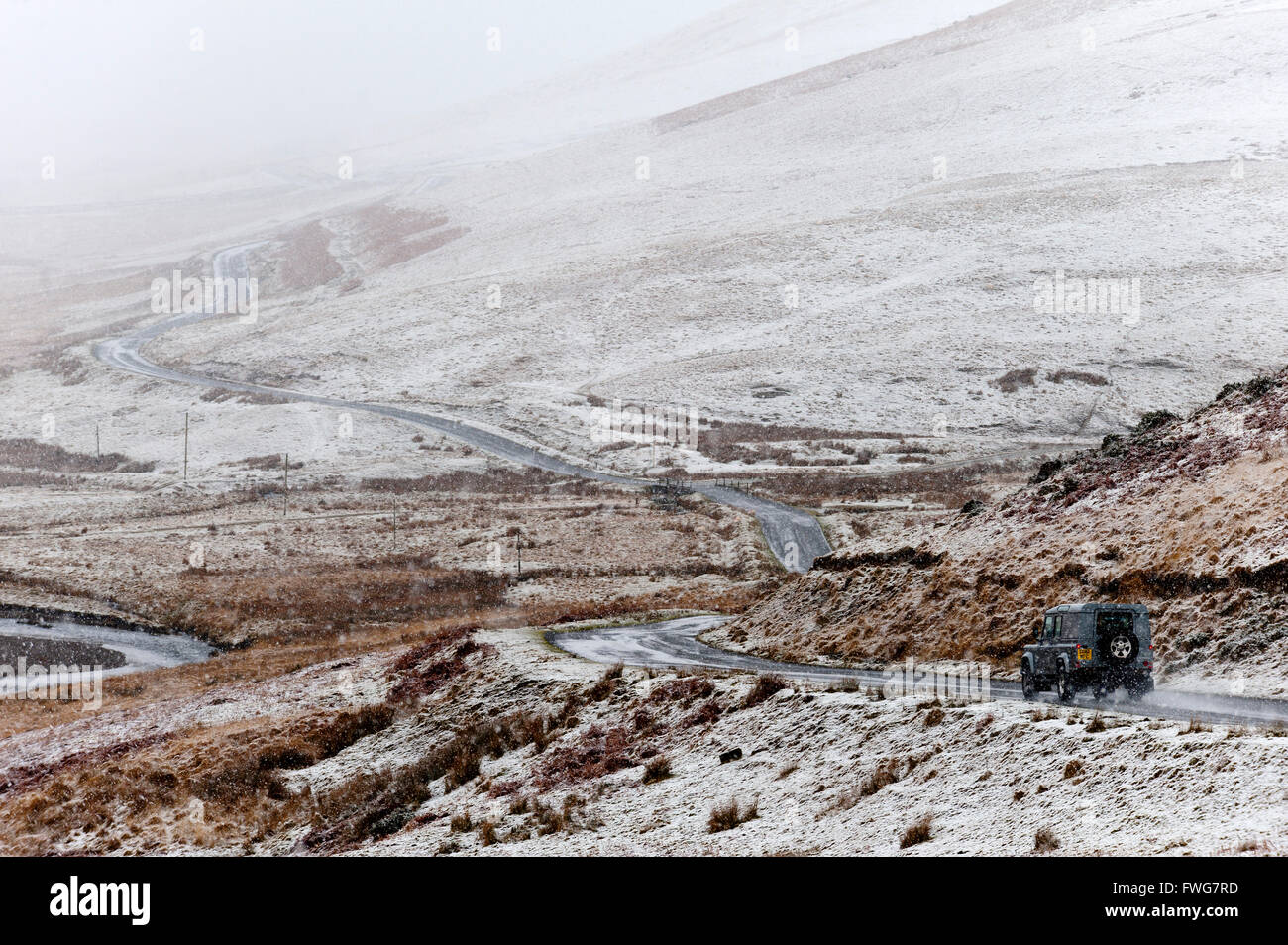 Un véhicule négocie une route à travers un paysage hivernal dans la région de la vallée de l'Elan en Powys, Pays de Galles, Royaume-Uni. Banque D'Images