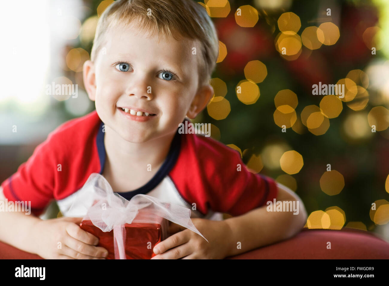 Un petit garçon par un arbre de Noël, la tenue d'un présent. Banque D'Images