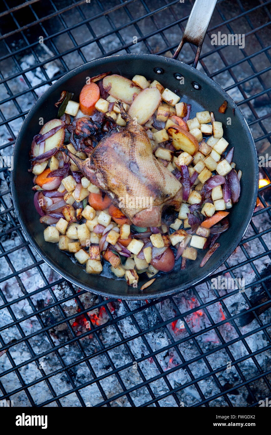 Une piscine en plein air, d'un gibier dans une casserole entouré de mirepoix de légumes au-dessus d'un feu rougeoyant. Banque D'Images