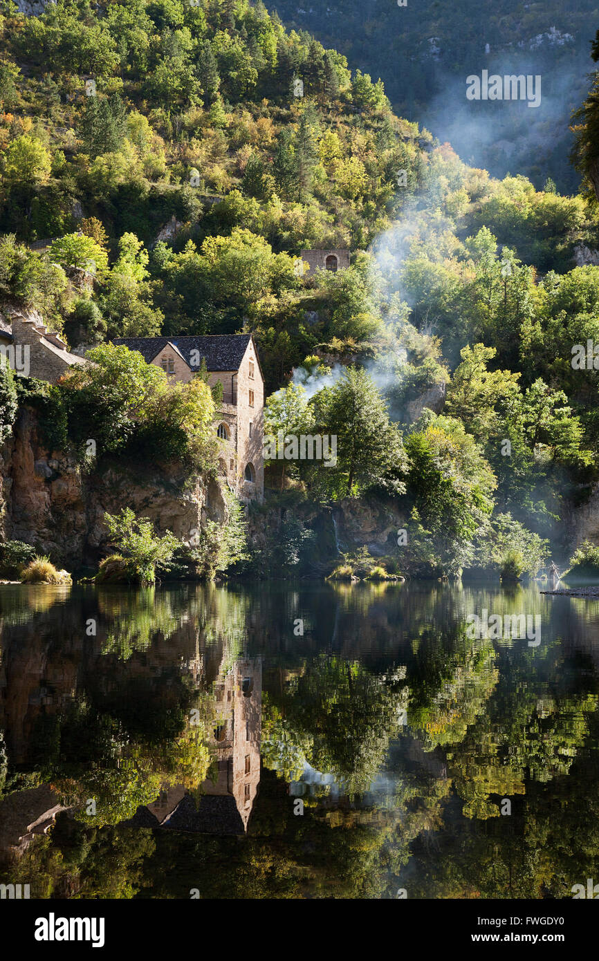 Maisons sur une colline escarpée, reflétée sur l'eau d'une rivière. La forêt, et un mince filet de fumée de bois augmente. Banque D'Images