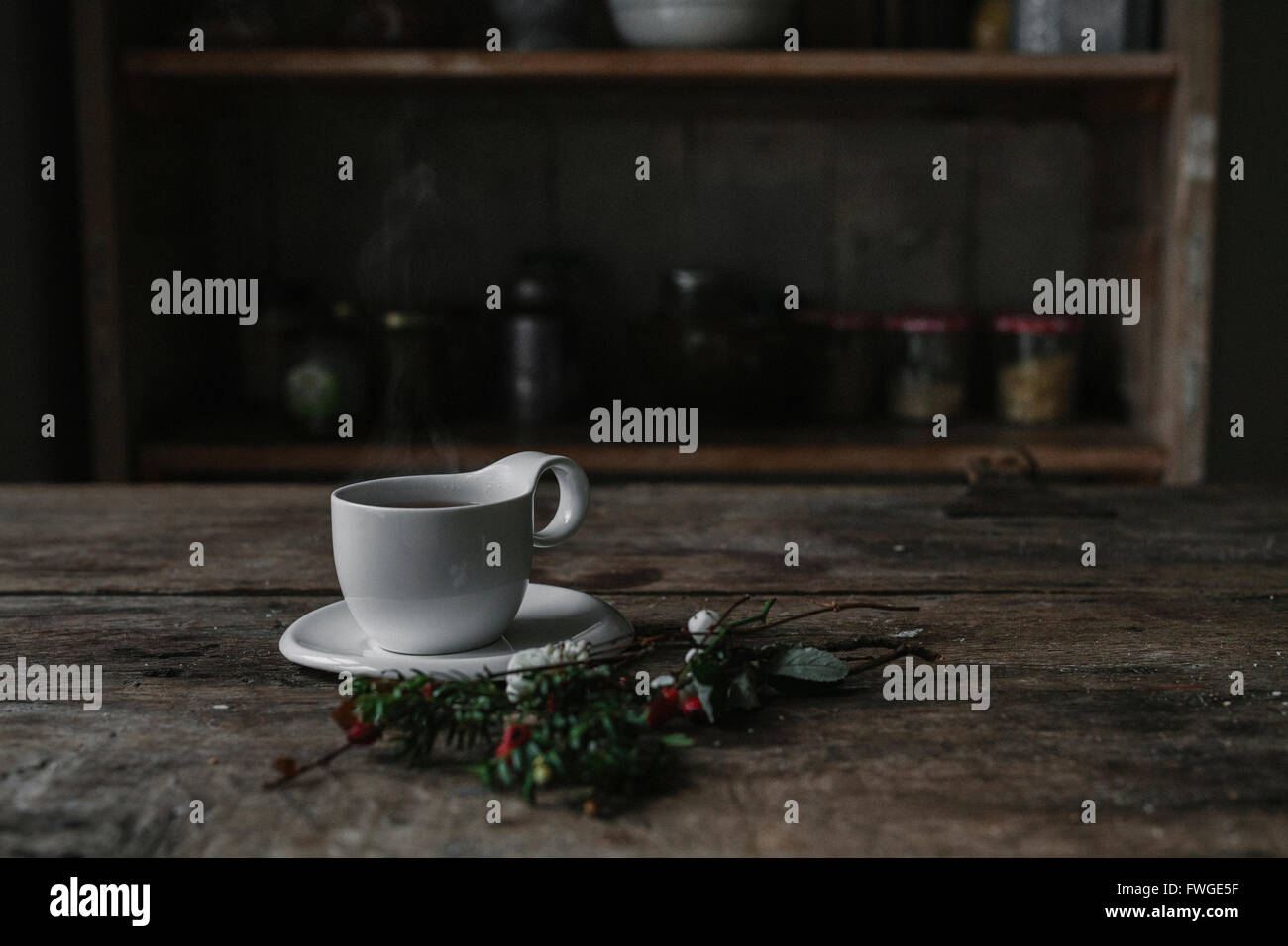 Une tasse et soucoupe en Chine blanc sur une table de cuisine et d'un rameau de pin et de baies. Banque D'Images