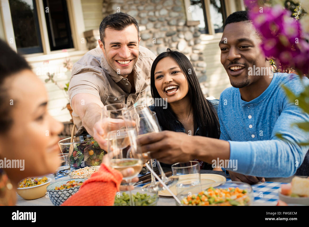 Autour d'une table d'amis, hommes et femmes de rire et de tintement des verres à vin dans un toast. Banque D'Images