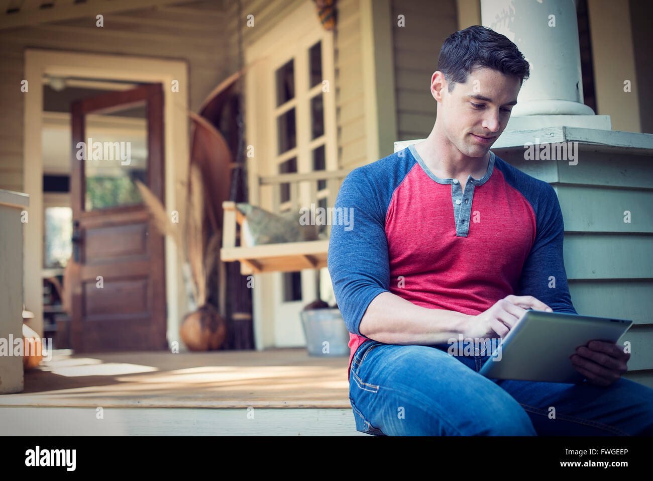 Un homme assis dans un coin tranquille de détente d'un porche, à l'aide d'une tablette numérique. Banque D'Images