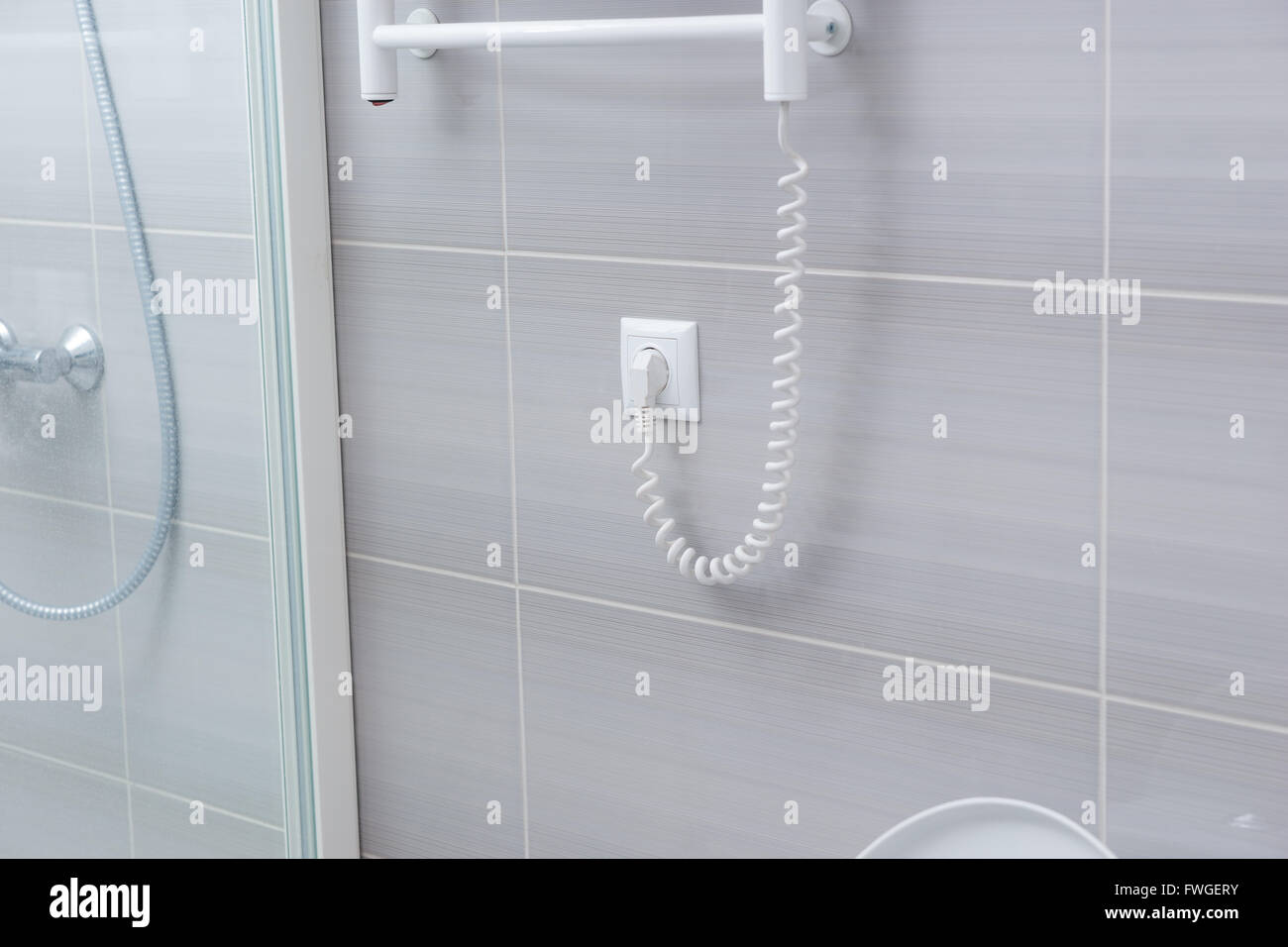 Vue détaillée de forme de spirale cordon d'une grille chauffante pour la serviette branché sur mur avec des carreaux gris Banque D'Images