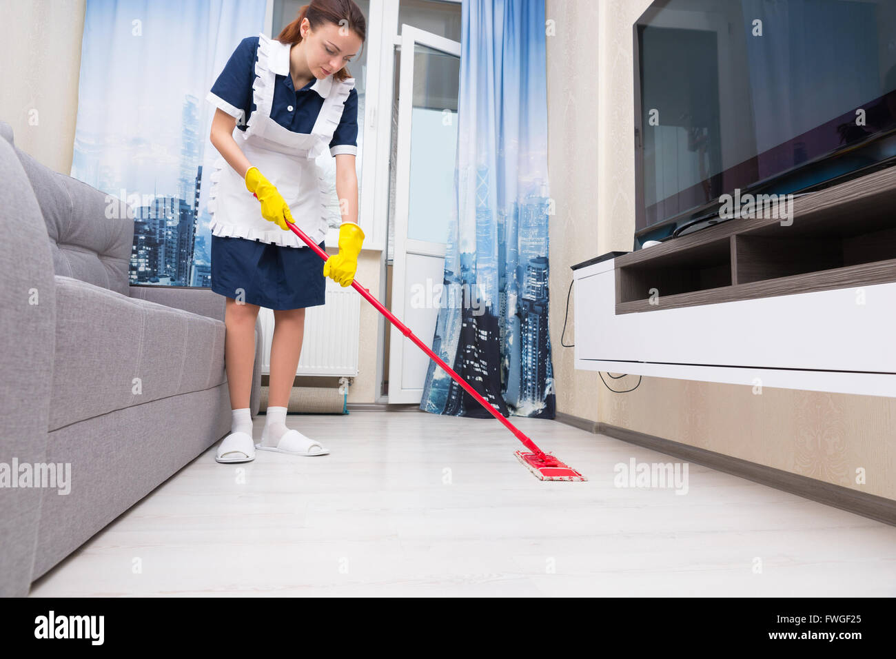 Femme de ménage ou une aide ménagère dans un tablier blanc pur le nettoyage  d'un salon avec un rouge coloré rdp, low angle view au niveau du sol Photo  Stock - Alamy