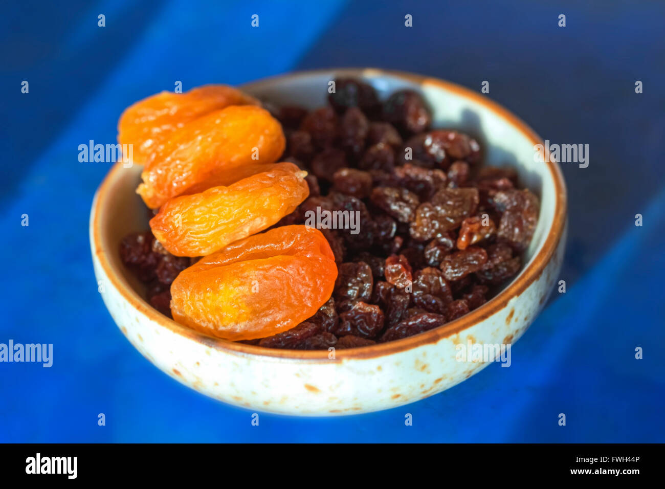 Abricots secs et raisins secs dans peu de plaque sur fond bleu Banque D'Images