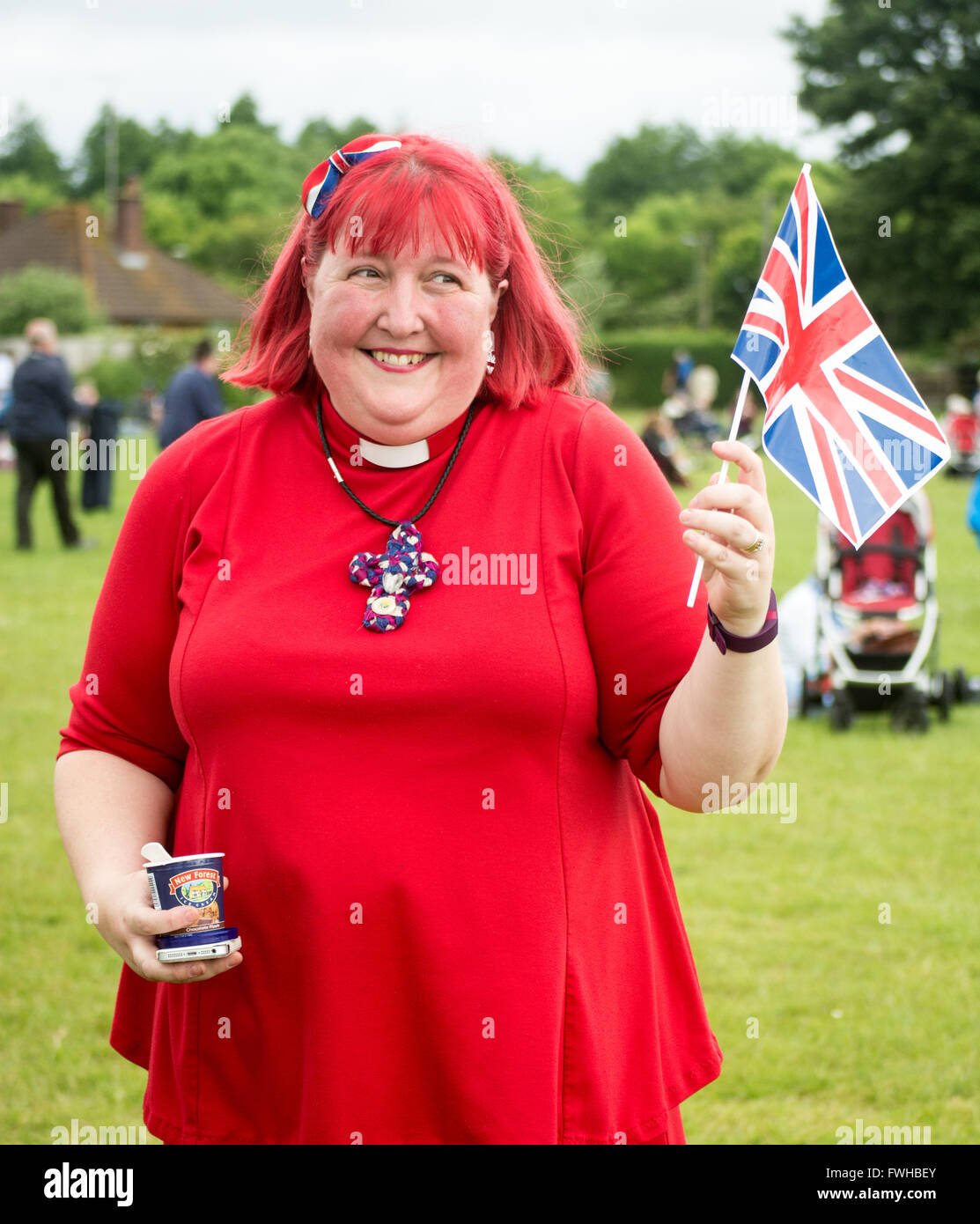 Vicaire de l'église d'Angleterre portant une robe rouge et brandissant un drapeau Union Jack au cours de la Reine pour le 90e anniversaire de la ville de New Forest, Hampshire, Royaume-Uni Fordingbridge Banque D'Images
