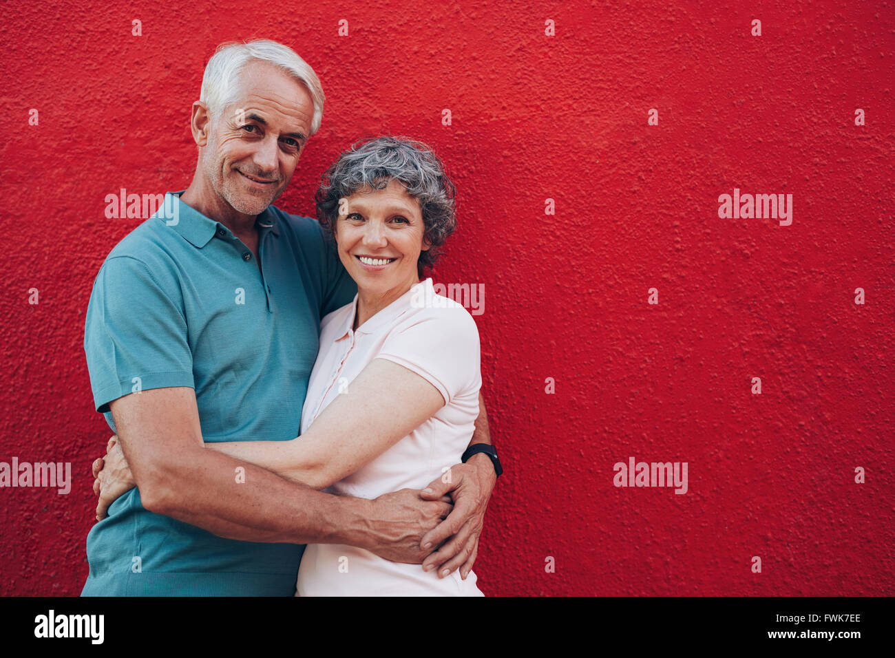 Portrait d'aimer middle aged man and woman standing ensemble contre l'arrière-plan rouge. Senior couple embracing contre mur rouge Banque D'Images