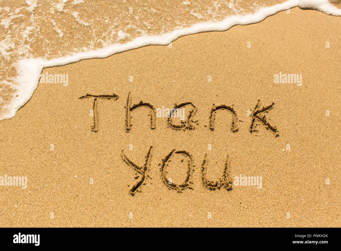 Merci - écrit manuellement sur la texture du sable de la mer, avec l'onde. Banque D'Images